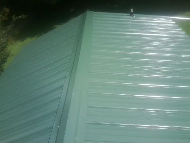 New green metal panels meeting at the ridge of a roof — Flat Roof Repair work by our crew in Staten Island