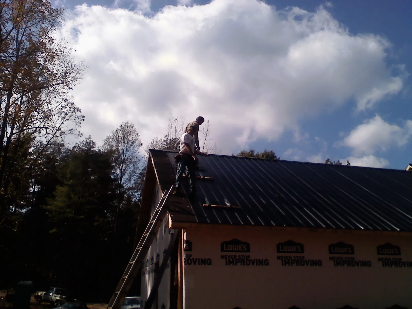 Roofer fastening dark metal panels high against a cloudy sky, from a Roof Inspection job in Staten Island