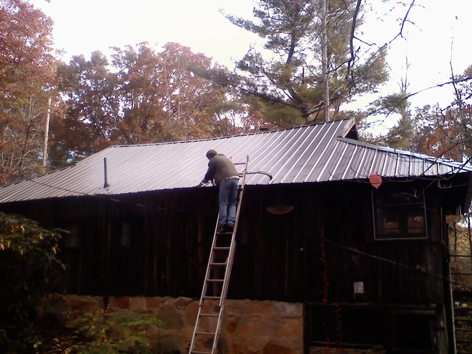 Roofer on a ladder working along the edge of a cabin metal roof in Staten Island