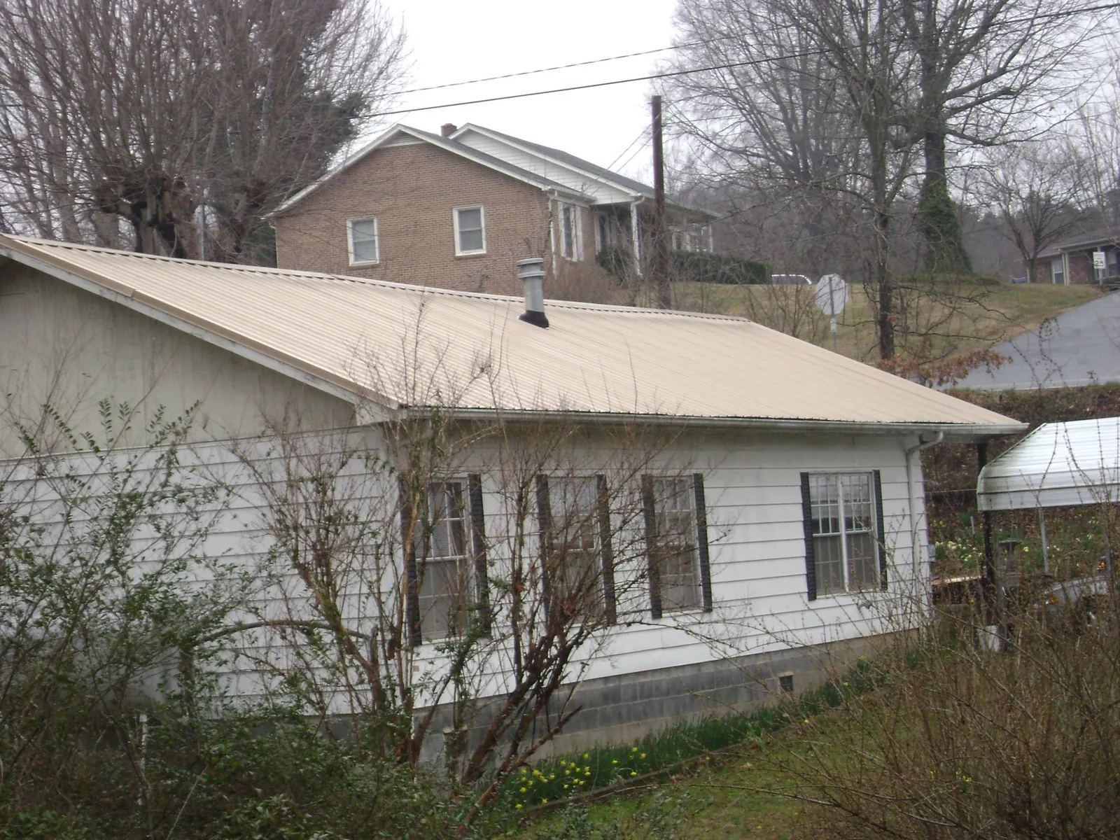 Tan metal roof on a white sided house set into a hillside — Commercial Roofing by Roofing Brothers in Staten Island